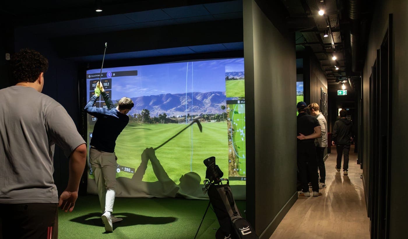 Colleagues watching a teammate swing in a bay at Caddi Club Fulham
