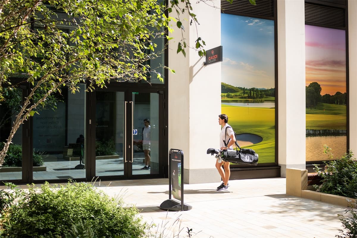 A golfer with his bag arriving at Caddi Club Waterloo, past the golf course mural